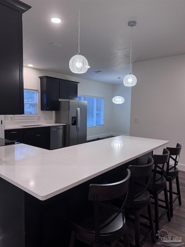 kitchen with pendant lighting, stainless steel fridge, dark hardwood / wood-style floors, and a kitchen bar