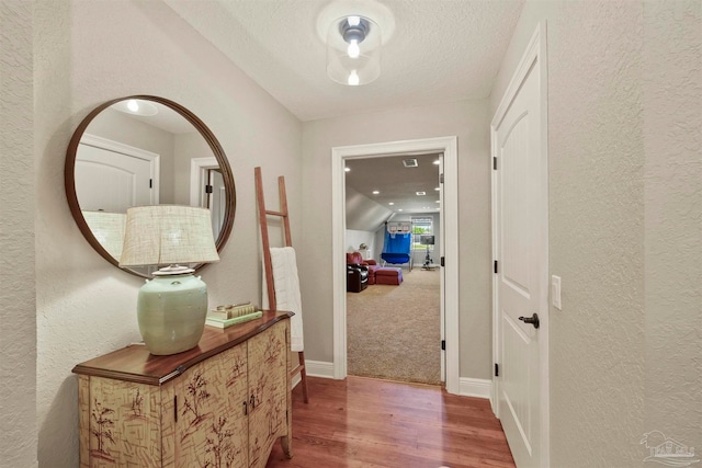 hall with lofted ceiling, wood-type flooring, and a textured ceiling