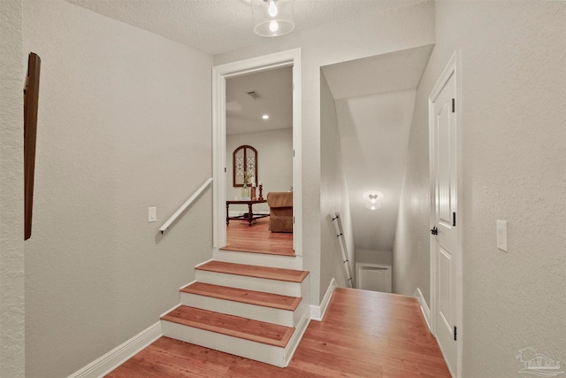 staircase with hardwood / wood-style floors and a textured ceiling