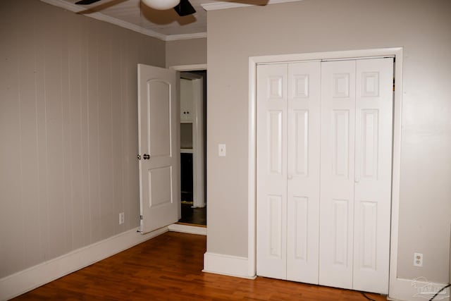 unfurnished bedroom featuring wood walls, hardwood / wood-style flooring, ceiling fan, ornamental molding, and a closet