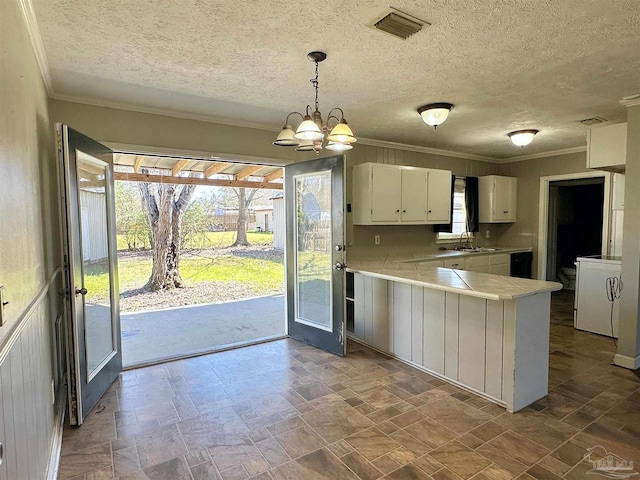 kitchen featuring washer / dryer, a peninsula, hanging light fixtures, light countertops, and white cabinetry