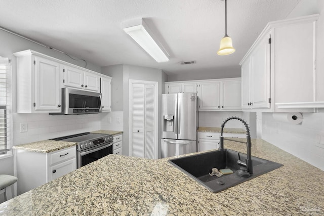 kitchen with appliances with stainless steel finishes, white cabinetry, sink, backsplash, and hanging light fixtures