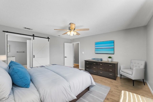 bedroom with ceiling fan, a barn door, and light hardwood / wood-style floors