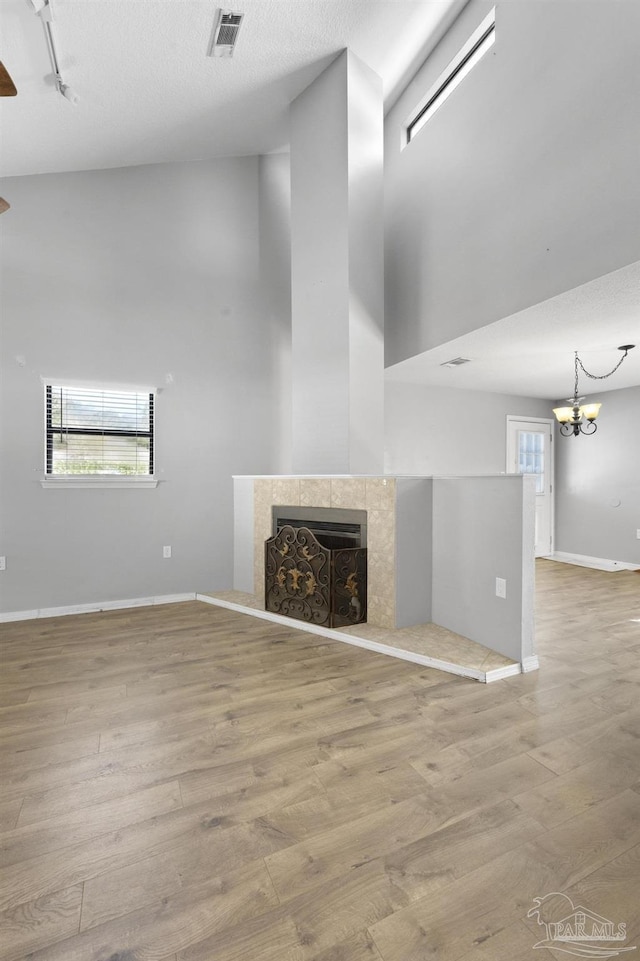 unfurnished living room with a towering ceiling, a fireplace, rail lighting, a chandelier, and light wood-type flooring