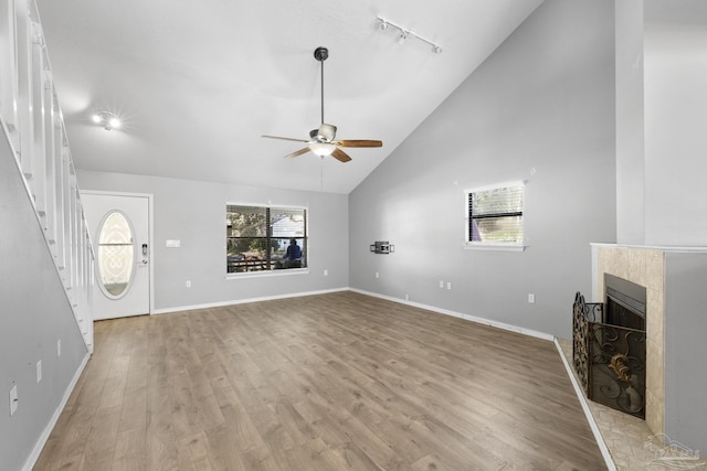 unfurnished living room featuring rail lighting, ceiling fan, a fireplace, high vaulted ceiling, and light hardwood / wood-style flooring