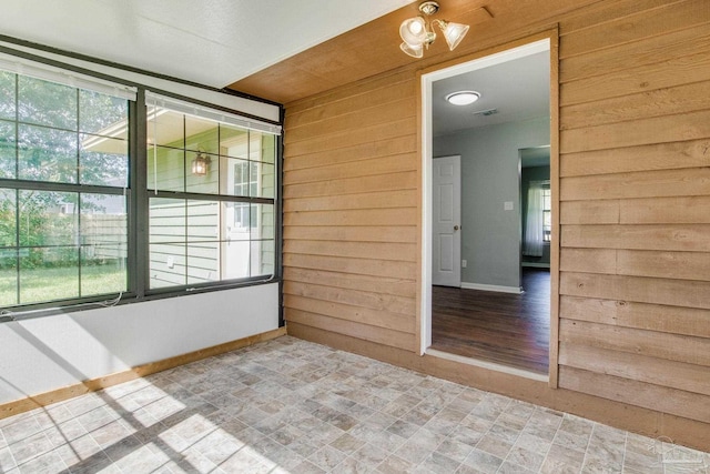 spare room featuring wood-type flooring, wood walls, and a healthy amount of sunlight