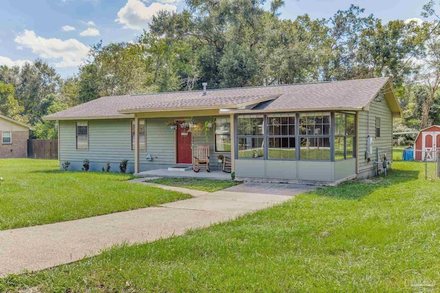 ranch-style home with a sunroom, a patio, a front lawn, and a shed