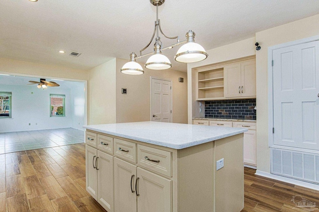 kitchen with a center island, dark wood-type flooring, decorative backsplash, hanging light fixtures, and ceiling fan