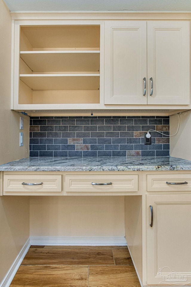 kitchen featuring cream cabinets, light hardwood / wood-style floors, built in desk, backsplash, and light stone counters