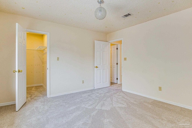 unfurnished bedroom featuring light colored carpet, a textured ceiling, a closet, and a spacious closet