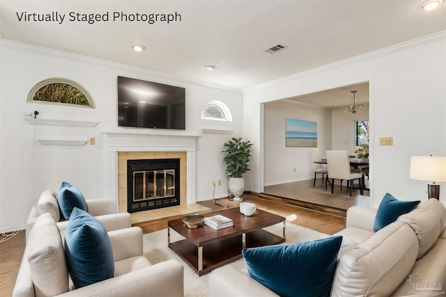 living room featuring wood-type flooring, a tiled fireplace, and ornamental molding