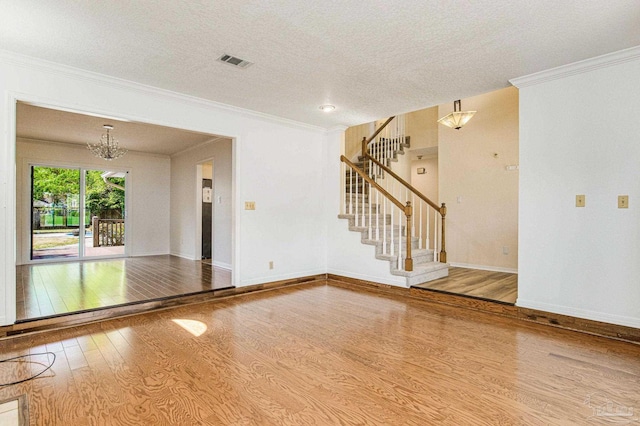 unfurnished living room featuring hardwood / wood-style flooring, a textured ceiling, ornamental molding, and a notable chandelier