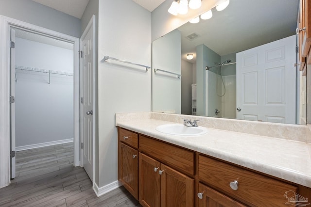 bathroom with wood finished floors, vanity, visible vents, a walk in closet, and walk in shower