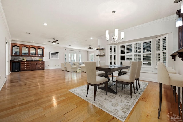 dining area with ceiling fan with notable chandelier, ornamental molding, wine cooler, and light hardwood / wood-style flooring