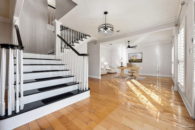 entryway featuring light wood-type flooring, ceiling fan with notable chandelier, and ornamental molding