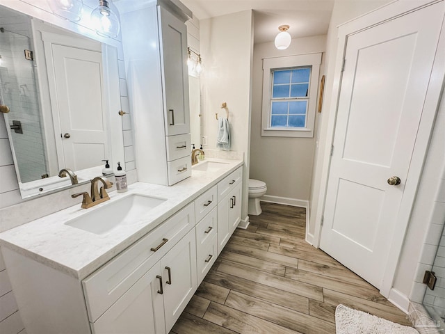 bathroom with double vanity, toilet, a sink, a shower stall, and wood finished floors