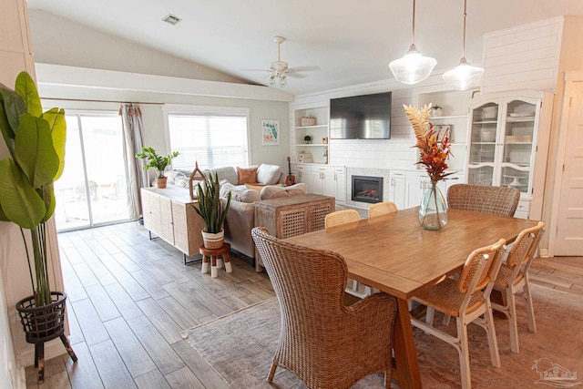 dining space featuring built in shelves, lofted ceiling, visible vents, a glass covered fireplace, and light wood-type flooring