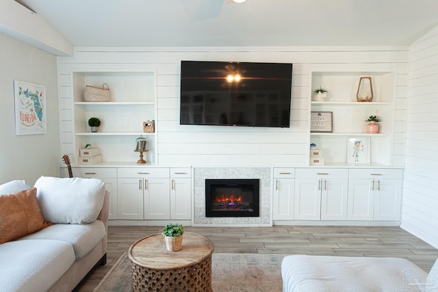 living room featuring light wood-style floors, built in features, and a glass covered fireplace