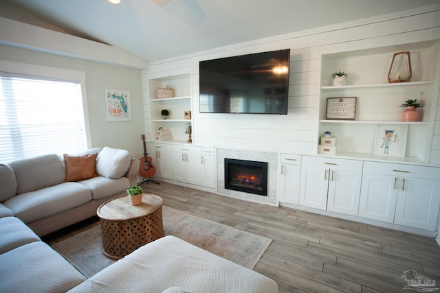 living room featuring light wood-style floors, lofted ceiling, a warm lit fireplace, and built in shelves