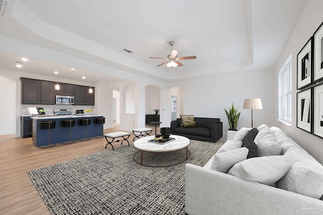 living room featuring a raised ceiling, ornamental molding, ceiling fan, and light wood-type flooring