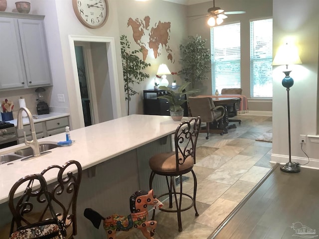 kitchen with ceiling fan, sink, light hardwood / wood-style flooring, and a kitchen breakfast bar