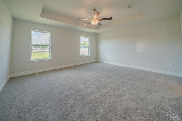 empty room featuring a raised ceiling, ceiling fan, and carpet floors