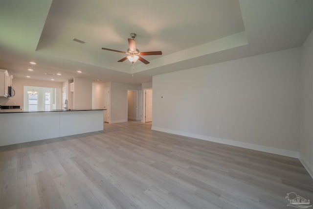 unfurnished living room featuring a raised ceiling, ceiling fan, and light hardwood / wood-style flooring