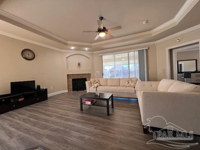 living room with crown molding, a fireplace, a tray ceiling, and ceiling fan