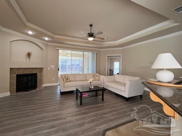 living room with dark hardwood / wood-style floors, ornamental molding, a tray ceiling, and a tile fireplace