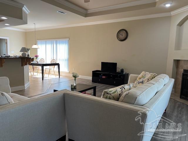 tiled living room with ornamental molding, a tiled fireplace, and a raised ceiling