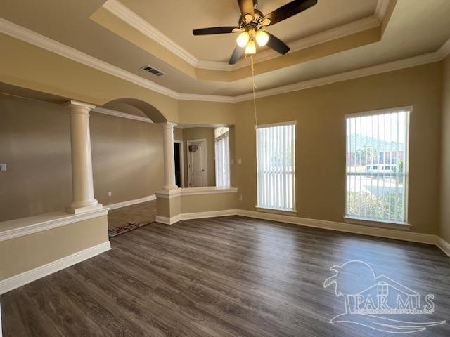 empty room with crown molding, a tray ceiling, and decorative columns