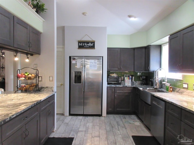 kitchen with sink, stainless steel appliances, dark brown cabinetry, light stone countertops, and light wood-type flooring