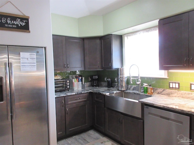 kitchen with appliances with stainless steel finishes, tasteful backsplash, sink, light stone counters, and dark brown cabinetry