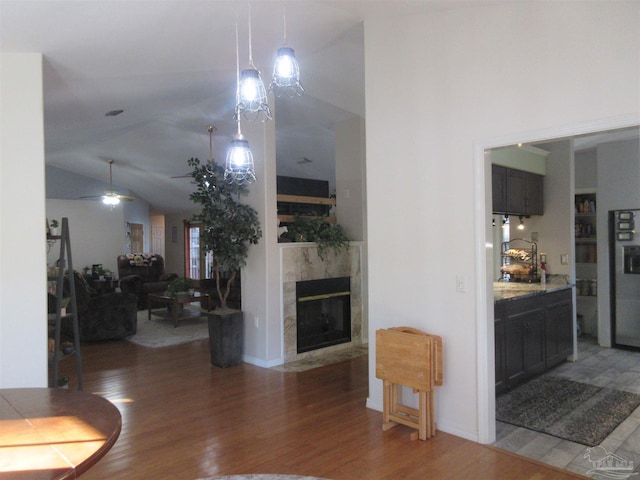 living room featuring a tile fireplace, vaulted ceiling, dark wood-type flooring, and ceiling fan