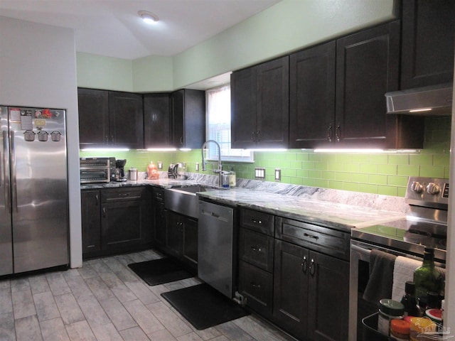 kitchen with tasteful backsplash, sink, light stone counters, light hardwood / wood-style floors, and stainless steel appliances