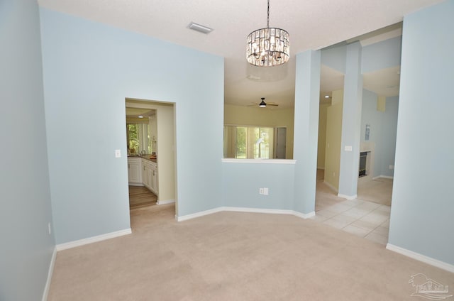 empty room featuring ceiling fan with notable chandelier and light colored carpet