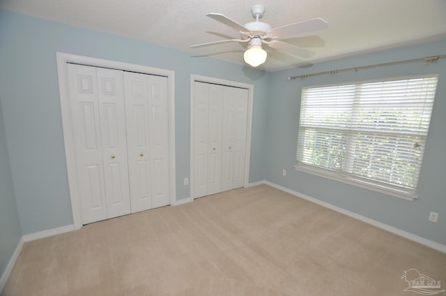 unfurnished bedroom featuring multiple closets, ceiling fan, and light colored carpet