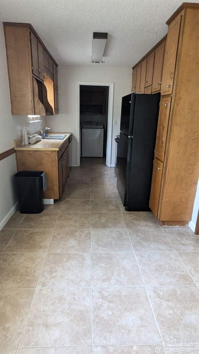 kitchen featuring sink, washer / clothes dryer, a textured ceiling, and black fridge