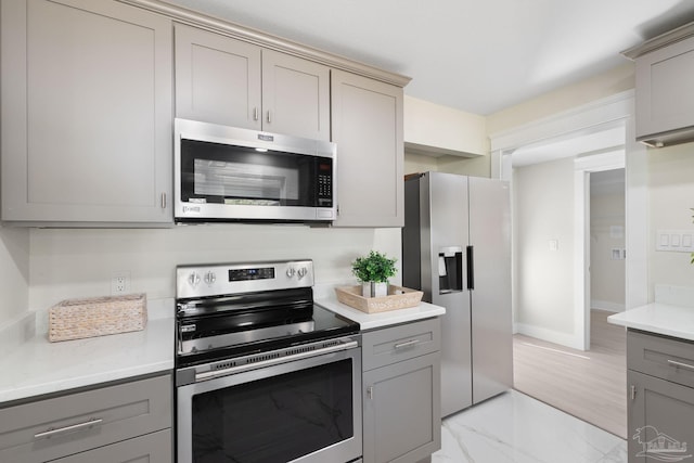 kitchen with baseboards, marble finish floor, appliances with stainless steel finishes, and gray cabinetry