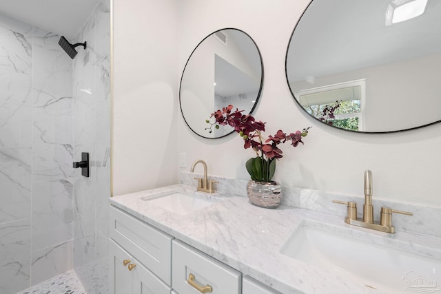 bathroom with a sink, a marble finish shower, and double vanity