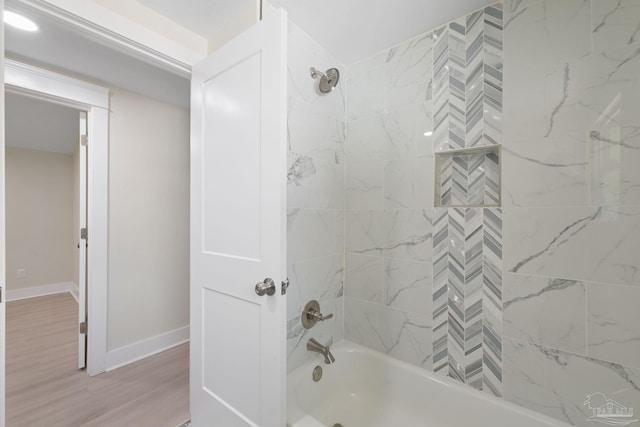 bathroom with wood finished floors, washtub / shower combination, and baseboards