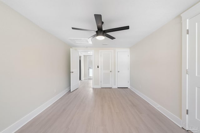 unfurnished bedroom with baseboards, a ceiling fan, attic access, and light wood-style floors