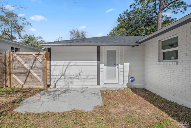 doorway to property featuring roof with shingles, a gate, fence, and brick siding