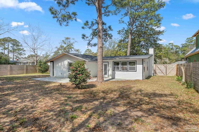 rear view of house with a chimney, a lawn, a gate, a patio area, and a fenced backyard