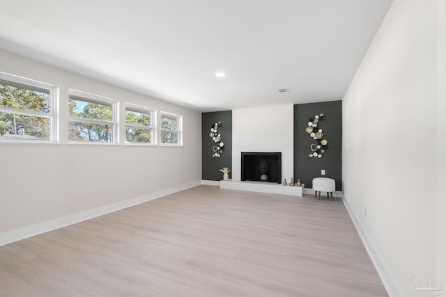 unfurnished living room with light wood-type flooring, visible vents, a fireplace, and baseboards