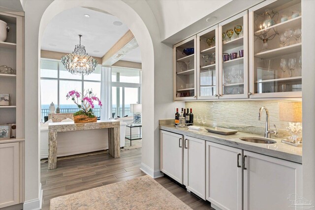 bar with light stone counters, white cabinets, dark hardwood / wood-style floors, and sink