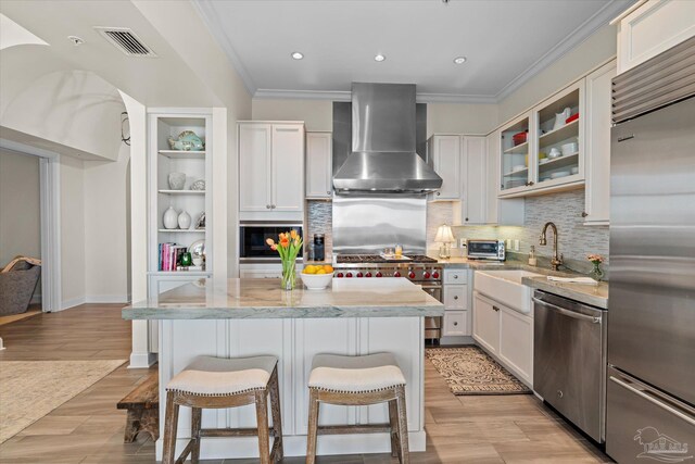 kitchen with wall chimney exhaust hood, premium appliances, light wood-type flooring, light stone counters, and white cabinetry