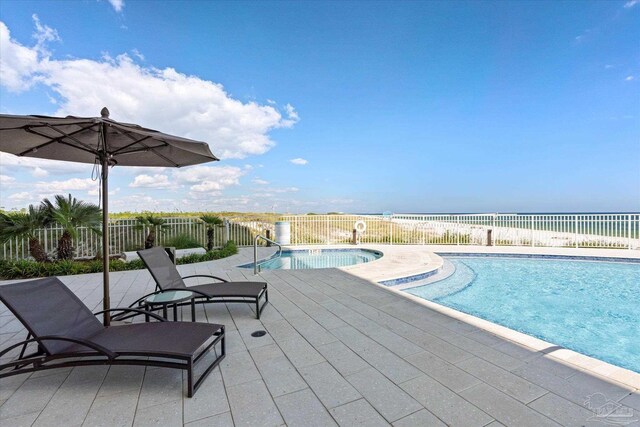 view of swimming pool with a water view, a beach view, and a patio area