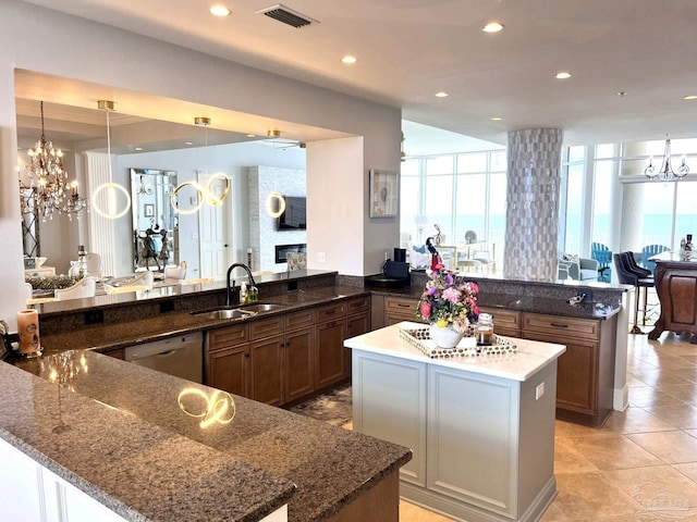 kitchen with a chandelier, kitchen peninsula, dark stone counters, sink, and a large fireplace