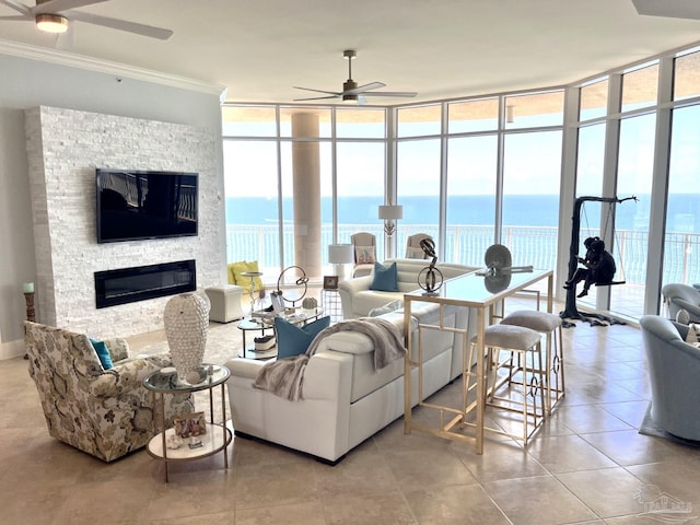 tiled living room with floor to ceiling windows, a water view, ceiling fan, a stone fireplace, and ornamental molding